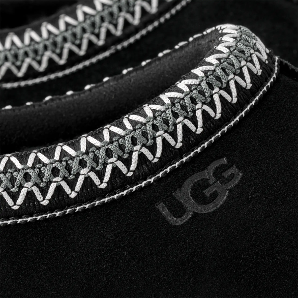 Close-up of the UGG Men's Tasman II Black suede upper with decorative white and gray stitching, featuring the embossed UGG logo—part of the classic collection.