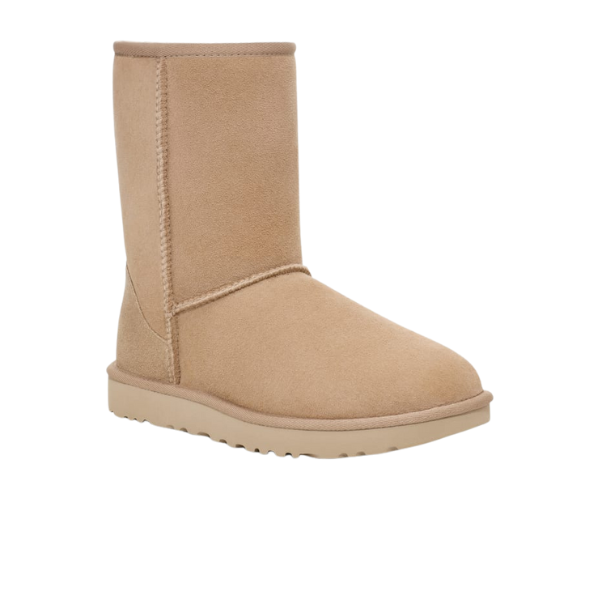 The UGG Womens Classic Short II Boots Sand, by UGG, feature tan suede with visible stitching, a textured rubber sole, and sheepskin lining for comfort. Shown mid-calf height on a white background.
