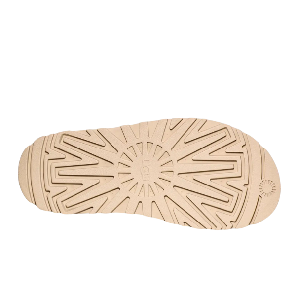 The UGG Womens Goldenglow Sandal Beige features a beige sole with a textured radial and geometric pattern, a central embossed UGG logo, and a sunburst design near the heel.