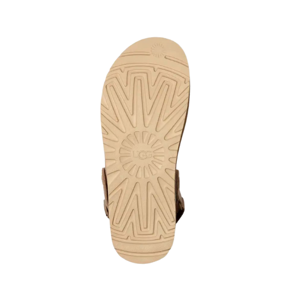 The image features the UGG Womens Goldenstar Clog Sand sole in light tan with a geometric tread and embossed UGG logo at the center, showcasing this comfortable footwear on a white background.