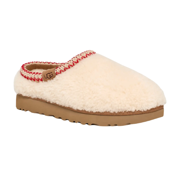 The UGG Women's Tasman Maxi Natural is a cream-colored, fluffy UGGplush slip-on slipper with a tan sole, red and white stitching around the opening, and a small brown UGG tag on the side.
